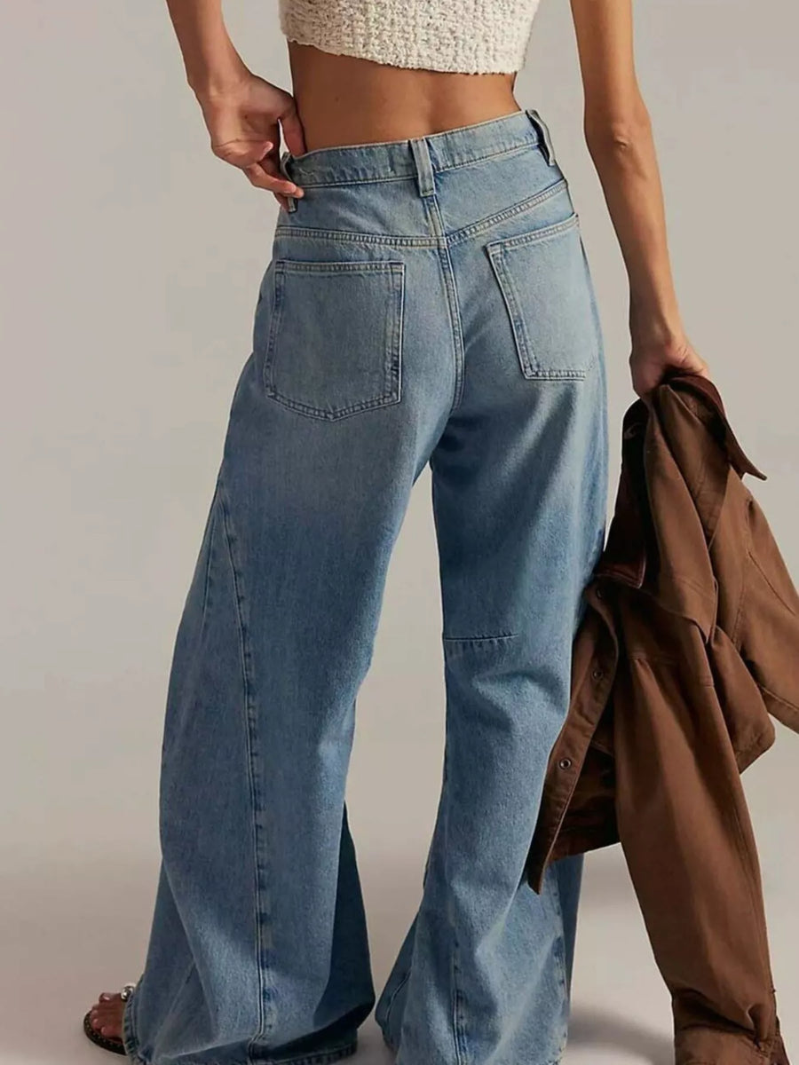 Person wearing blue jeans holding a brown jacket against a plain background