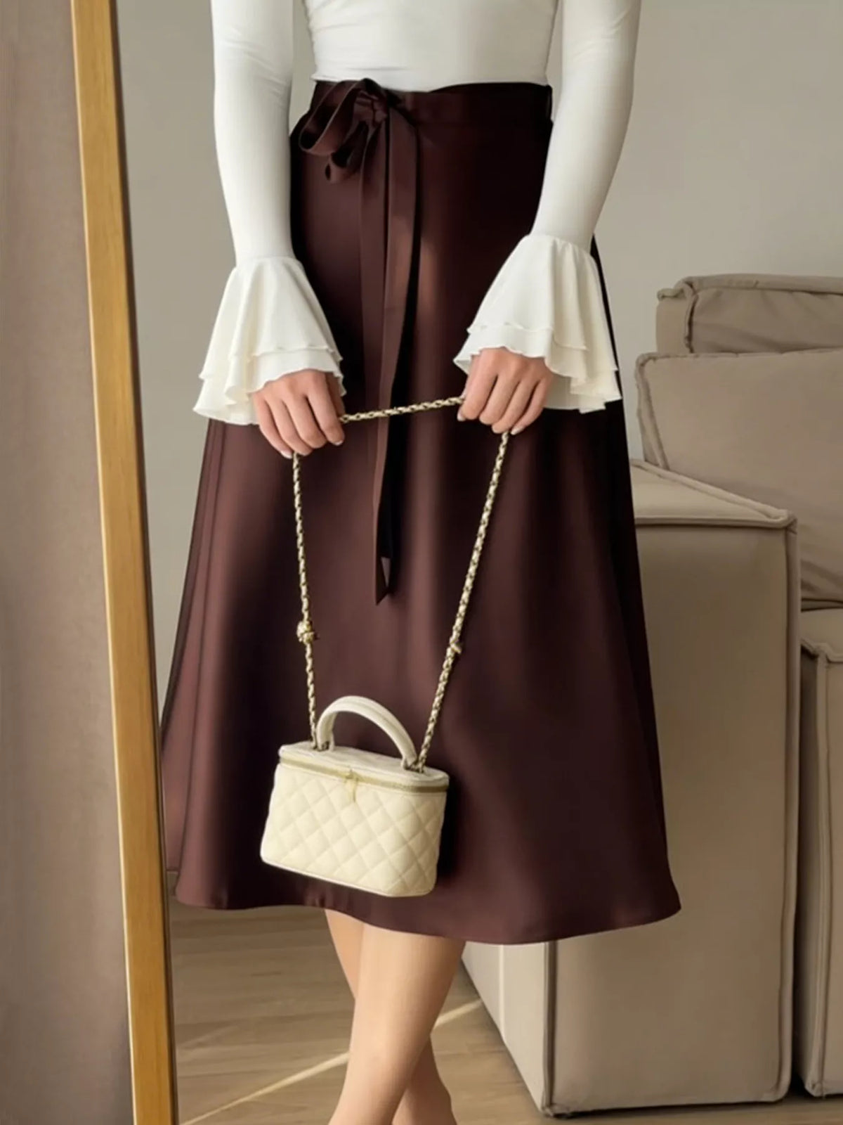 Person wearing a brown skirt and white top holding a cream-colored handbag.