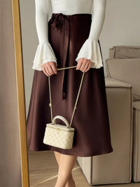 Person wearing a brown skirt and white top holding a cream-colored handbag.