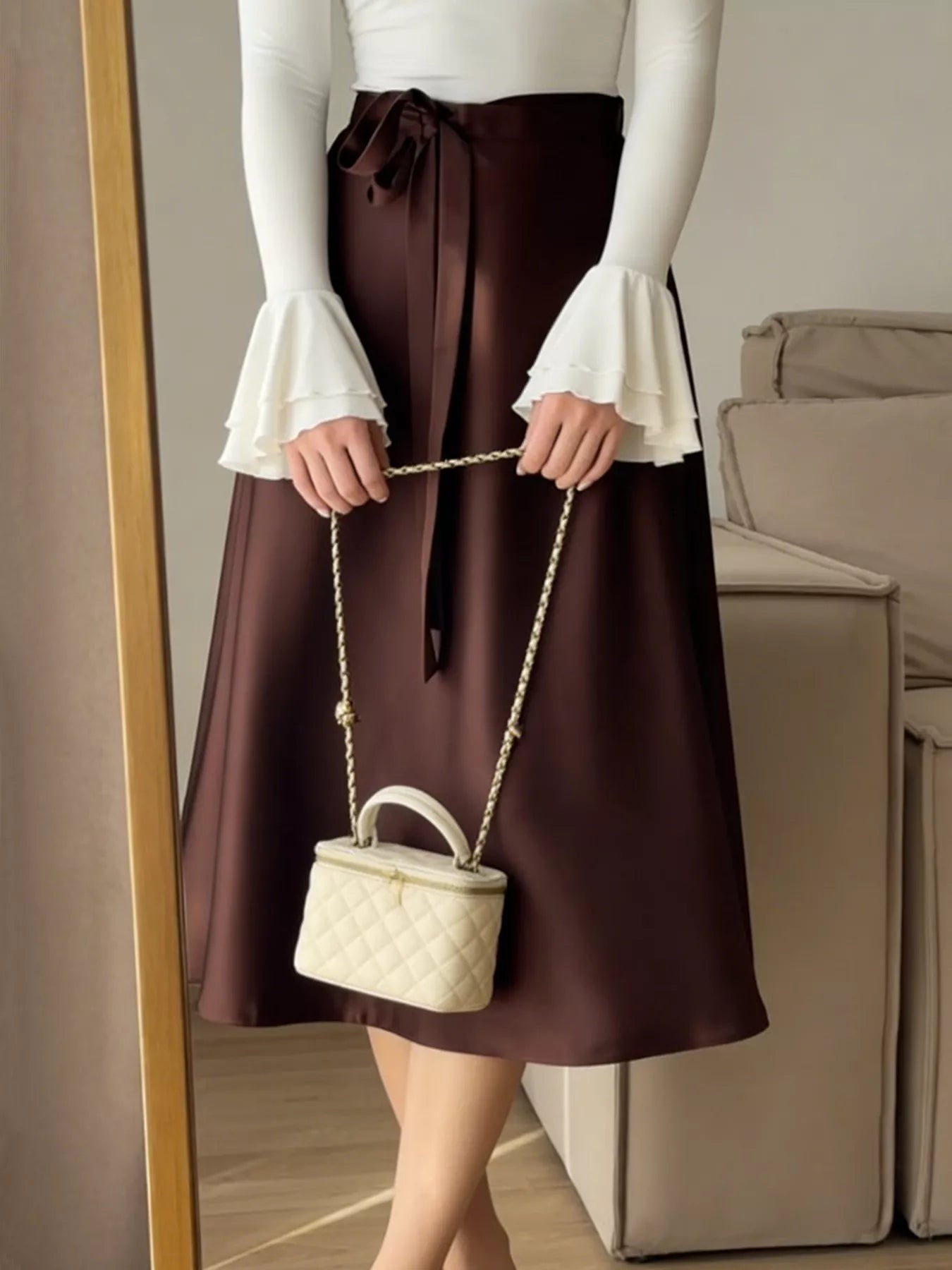 Person wearing a brown skirt and white top holding a cream-colored handbag.