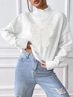 Person wearing a white sweater and light blue jeans against a white wall.