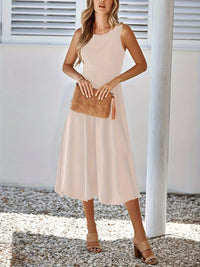 Woman wearing a beige sleeveless dress holding a brown clutch against a white background.