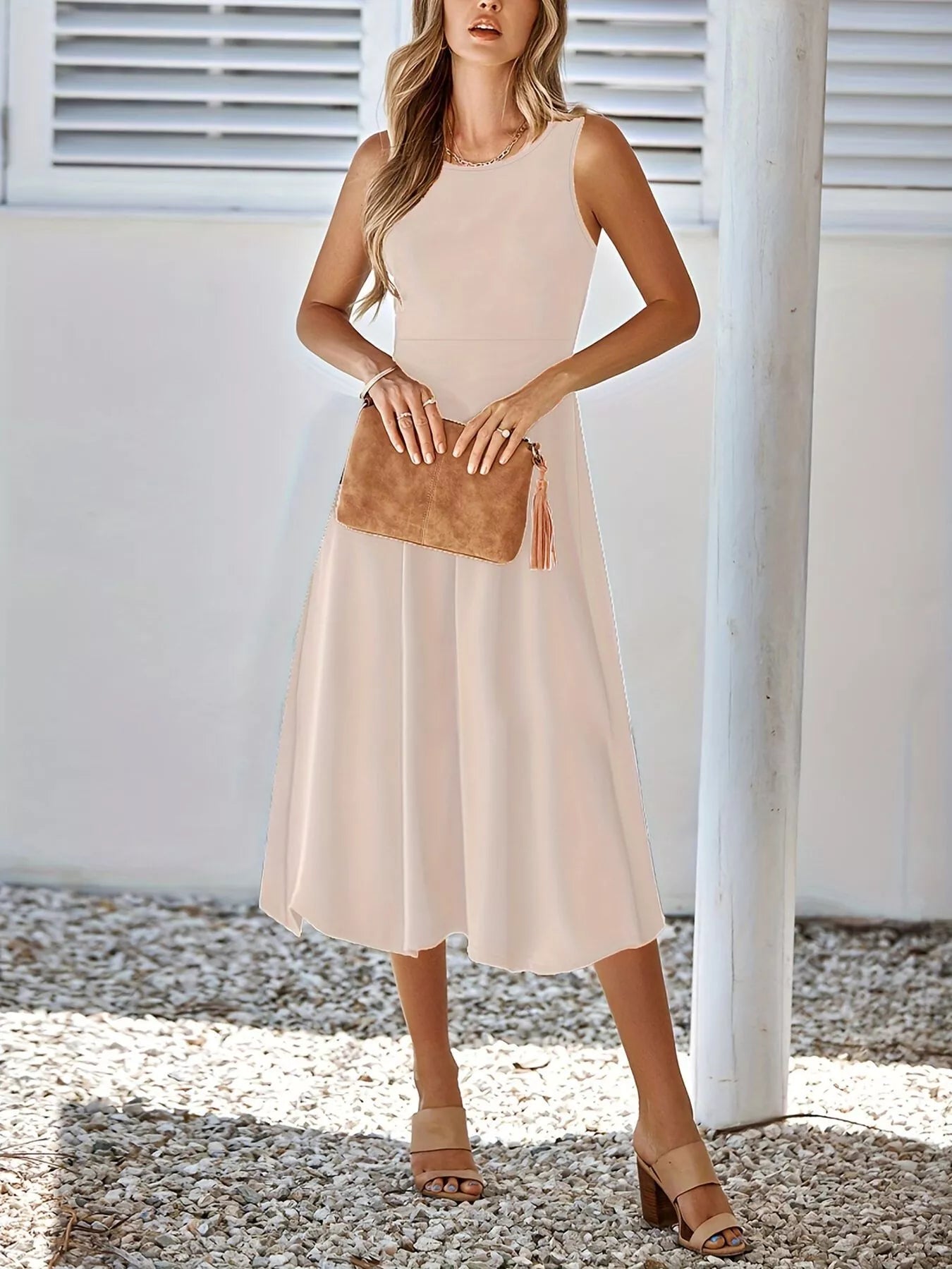 Woman wearing a beige sleeveless dress holding a brown clutch against a white background.
