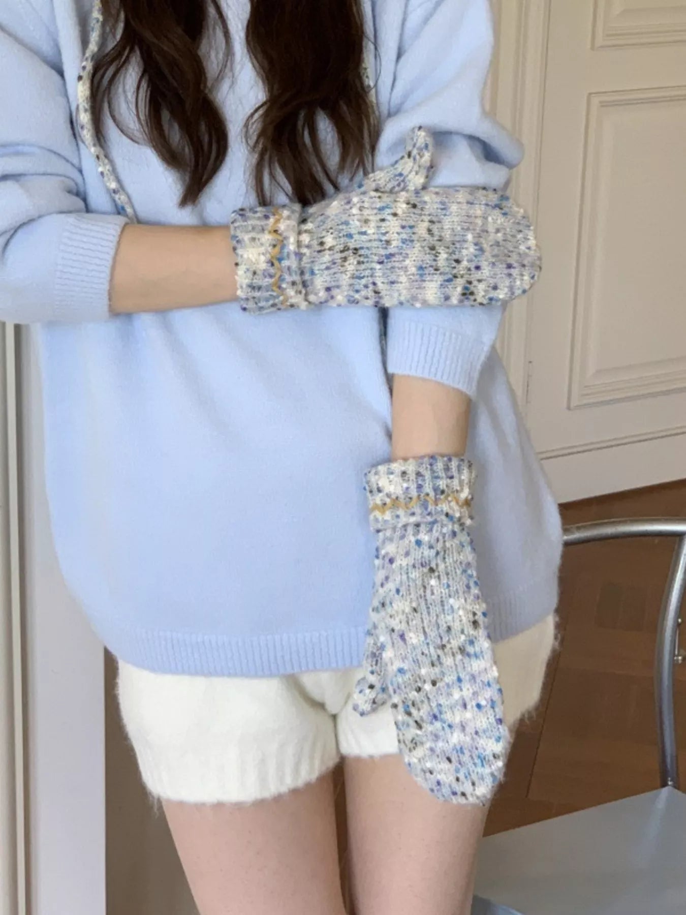 Person wearing a light blue sweater and white shorts with patterned gloves indoors.