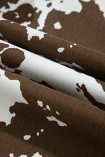 A close-up of draped fabric with a brown and white cow print pattern, showing the texture and folds of the material.