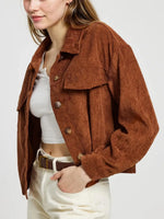Person wearing a brown corduroy jacket over a white top and pants on a plain background
