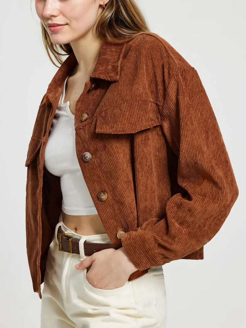 Person wearing a brown corduroy jacket over a white top and pants on a plain background