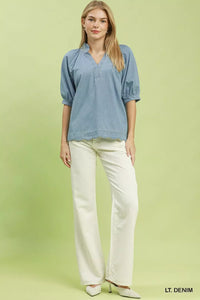 Woman wearing a light denim blouse and white pants on a green background
