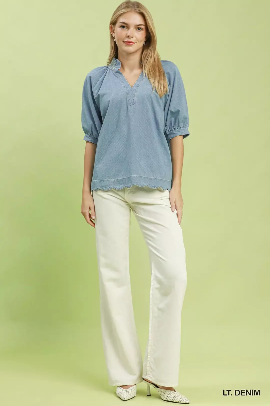 Woman wearing a light denim blouse and white pants on a green background