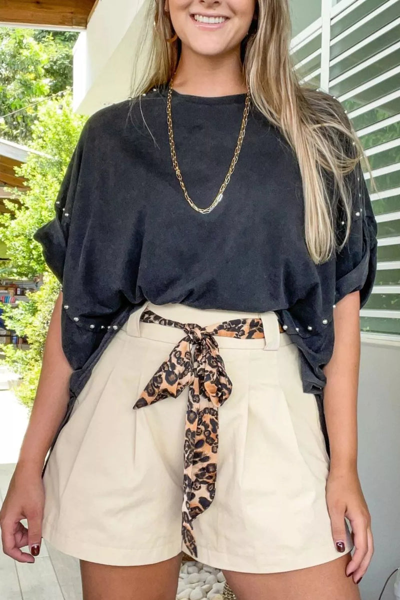 Woman wearing a black top and beige shorts with a leopard print tie, standing outdoors.