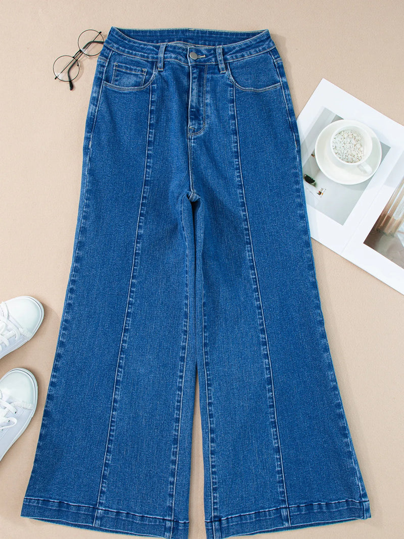 Blue jeans on a beige surface with white sneakers and glasses.