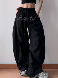 Black wide-leg pants with 'Pretty Girl' text worn by a person on a plain background