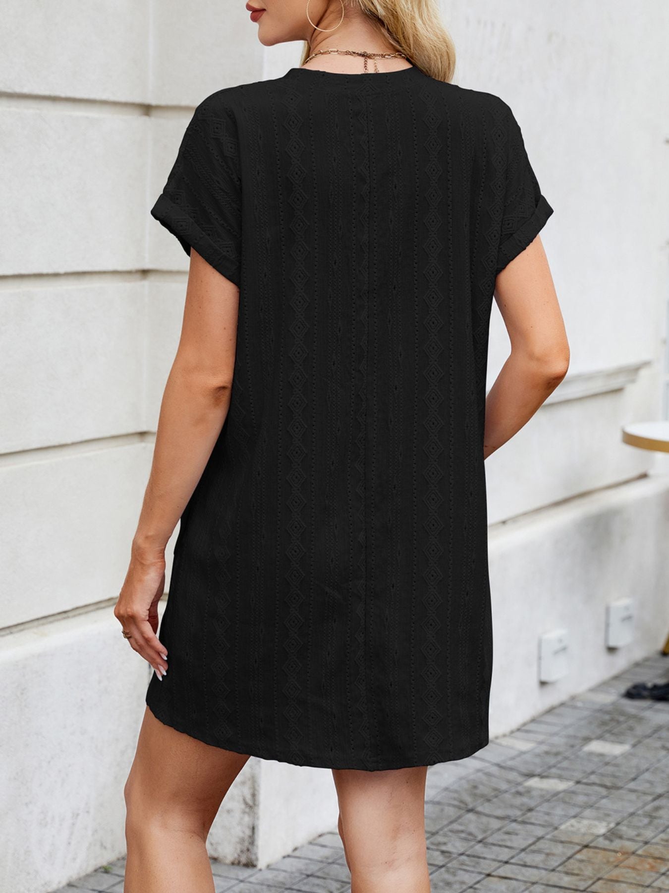 Person wearing a black t-shirt dress standing against a light-colored wall.