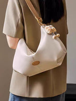 Beige handbag with teddy bear charm worn by a person in a beige coat.