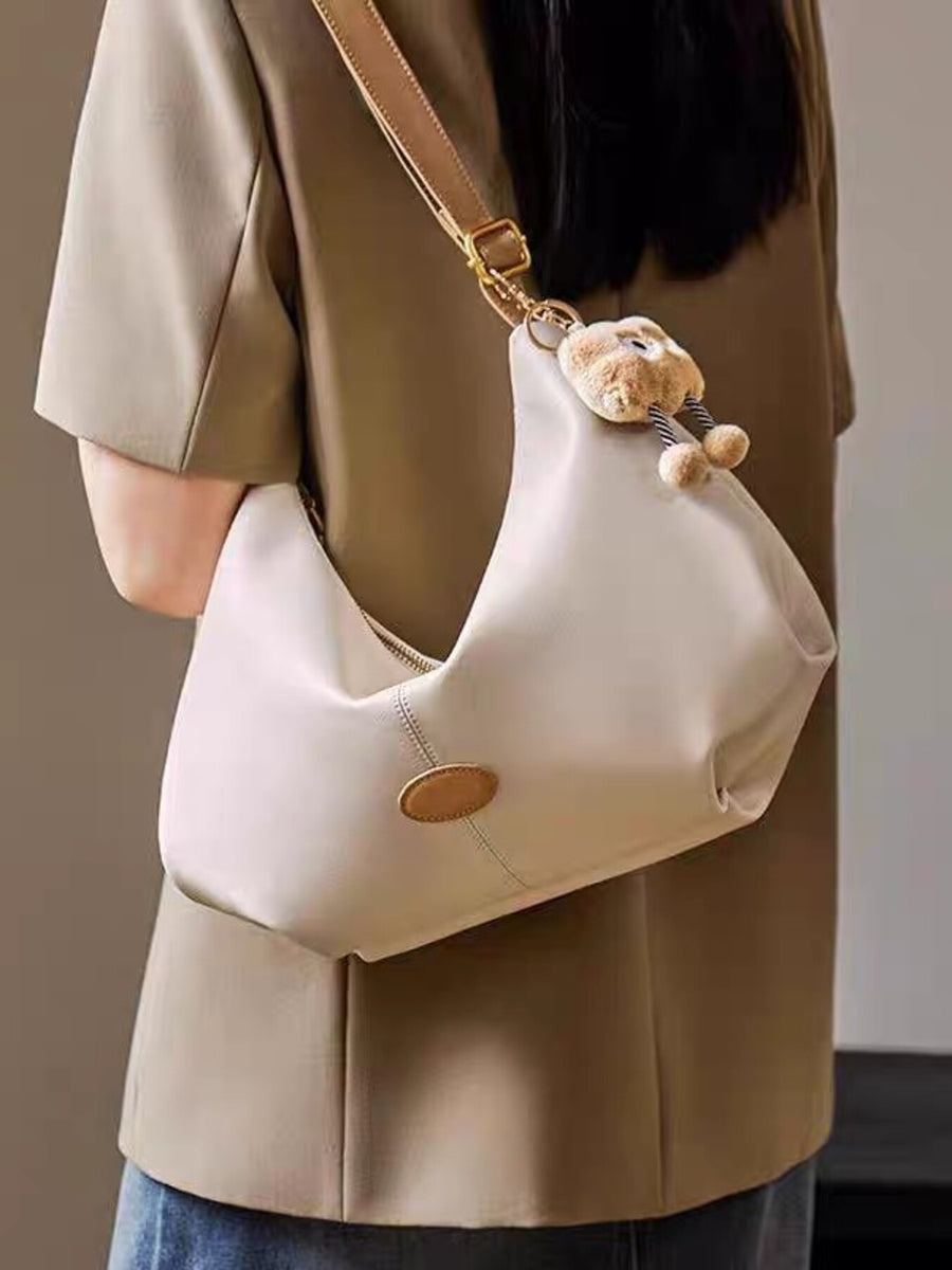 Beige handbag with teddy bear charm worn by a person in a beige coat.