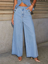 Person wearing a denim outfit with wide-leg jeans against a stone wall.