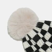 Black and white checkered knit hat with a large pom-pom on a light gray background