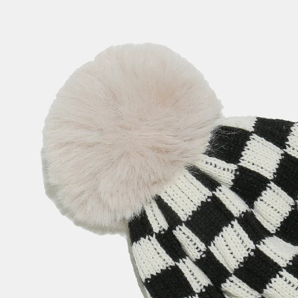 Black and white checkered knit hat with a large pom-pom on a light gray background