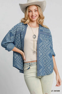 Woman wearing a blue patterned denim jacket, beige top, light green jeans, and a beige cowboy hat on a white background.