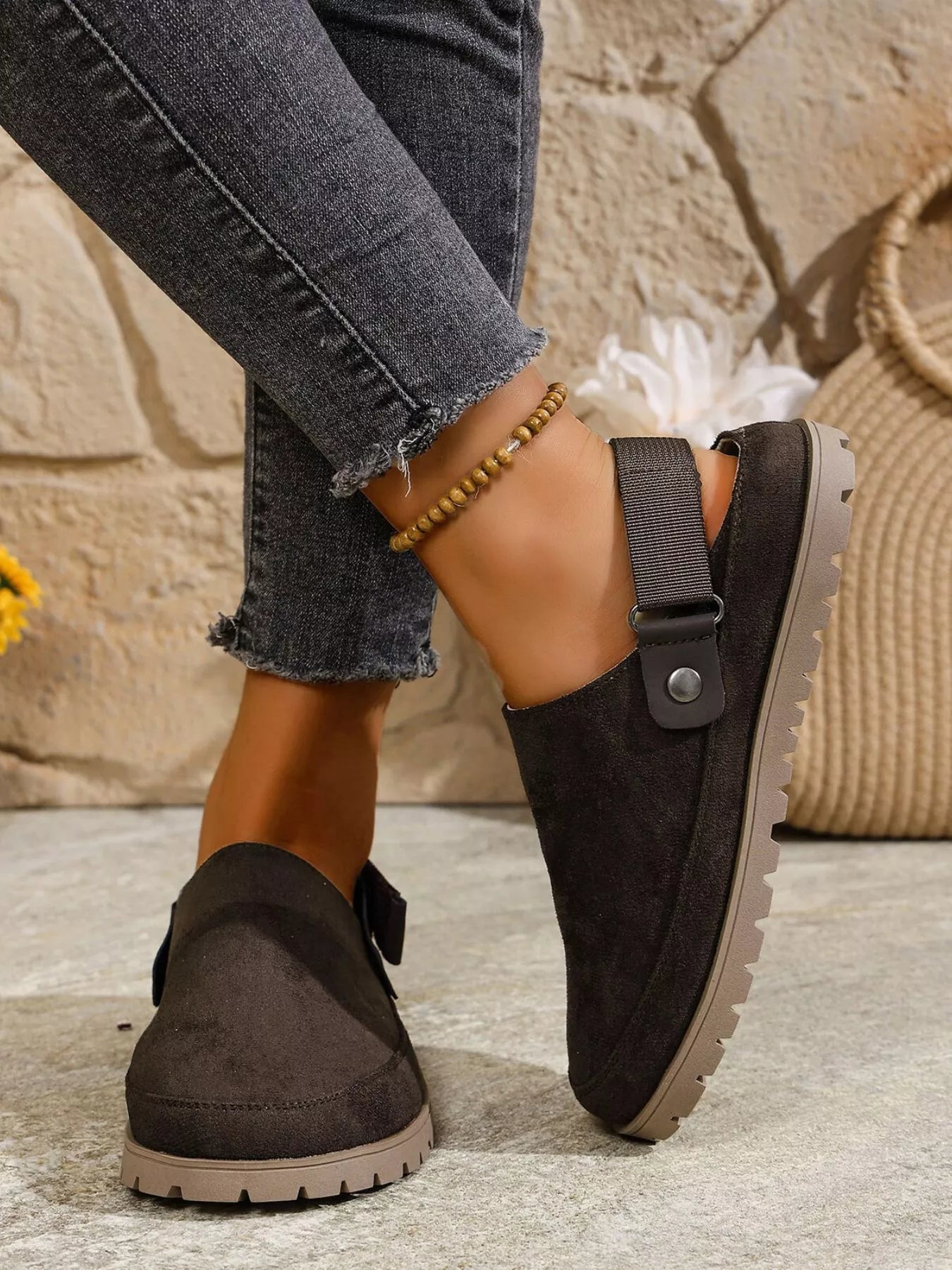 Person wearing black slip-on shoes with a stone wall background
