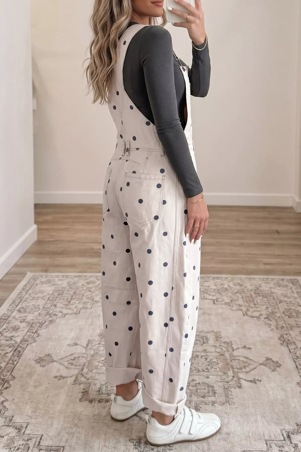 Woman wearing a polka dot jumpsuit in a room with wooden flooring and a patterned rug.