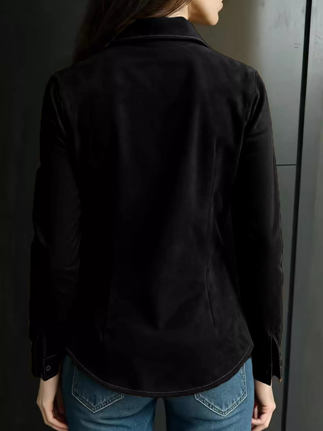 Person wearing a black jacket and blue jeans against a dark background