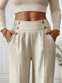 Person wearing beige high-waisted pants with button details and a cropped top.