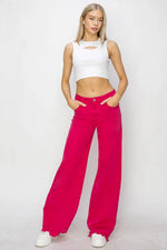 Woman wearing a white crop top and bright pink pants on a plain background