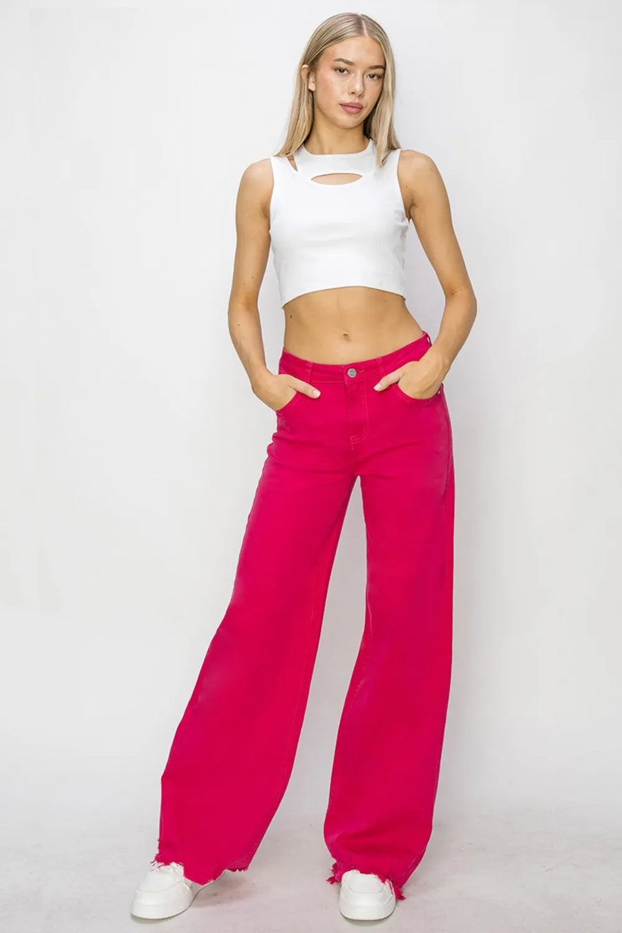 Woman wearing a white crop top and bright pink pants on a plain background