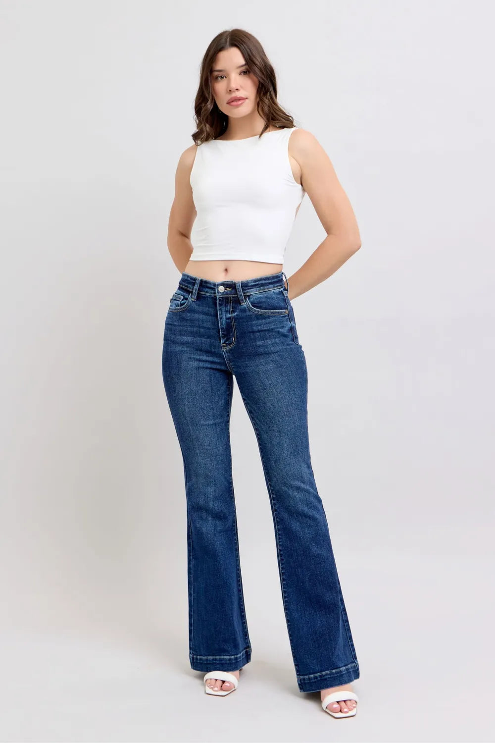 Woman wearing a white sleeveless top and blue jeans on a white background