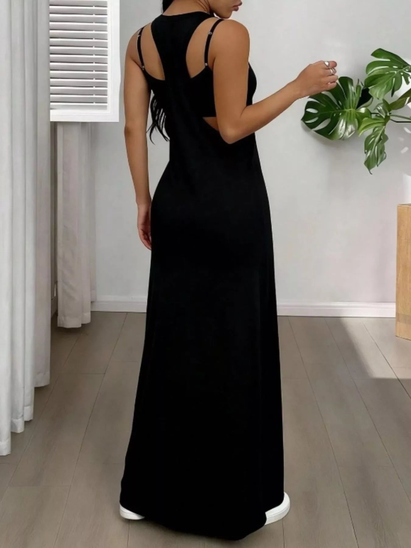 Woman wearing a black dress in a room with a plant and curtain.
