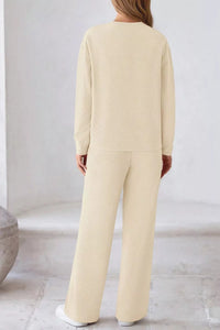 Person wearing a beige outfit with wide-leg pants in a minimalistic setting