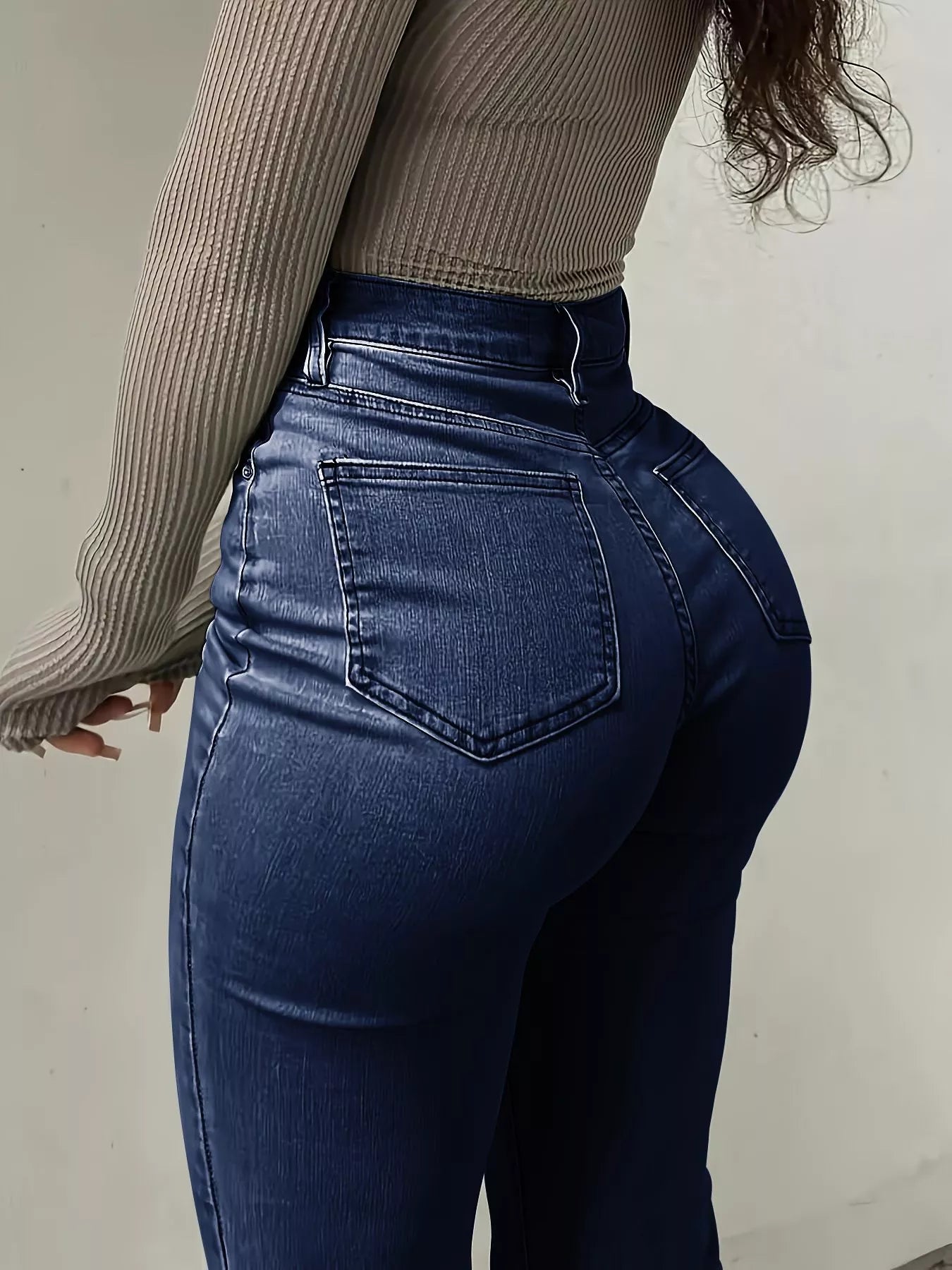 Person wearing blue jeans and a beige sweater from behind on a plain background