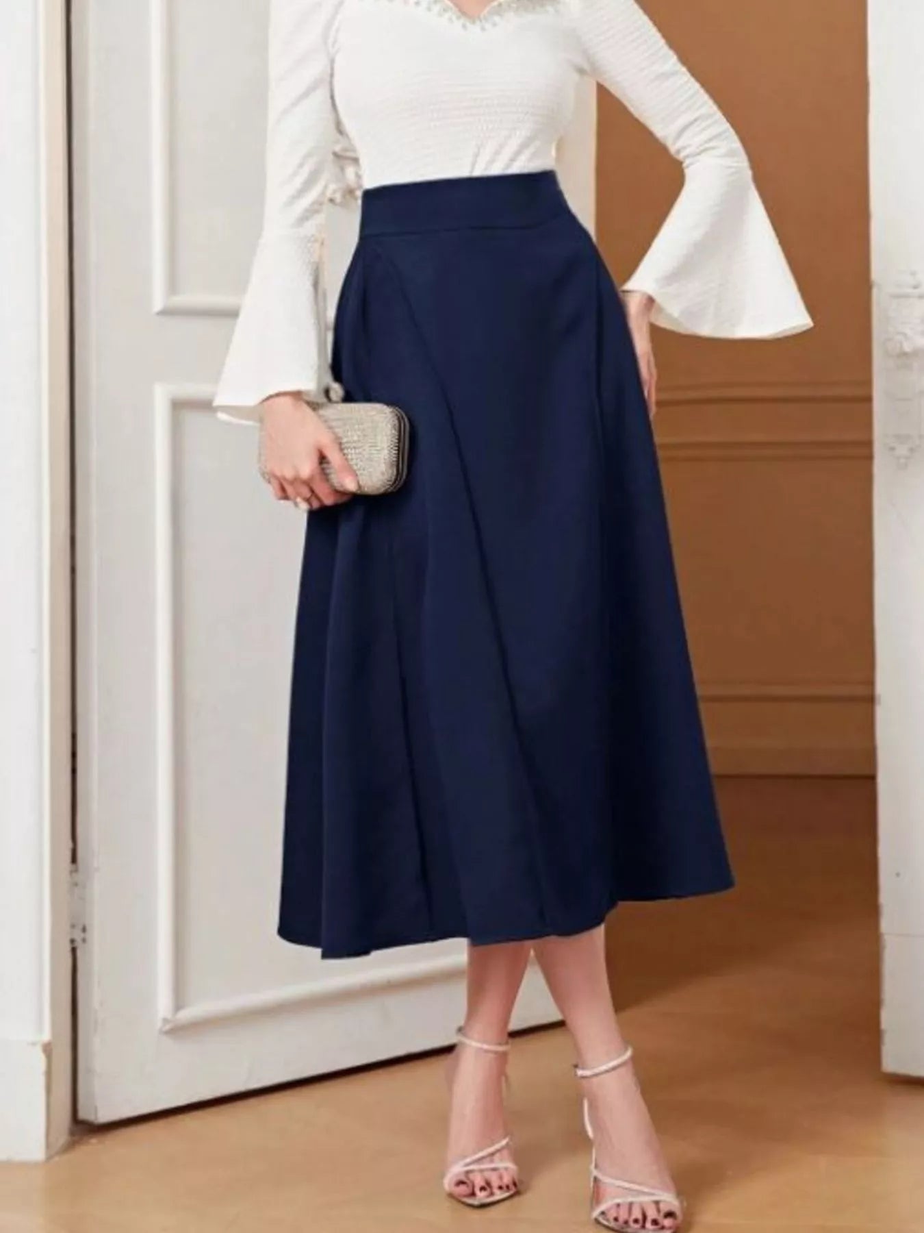 Person wearing a navy blue skirt with a white top and holding a clutch.