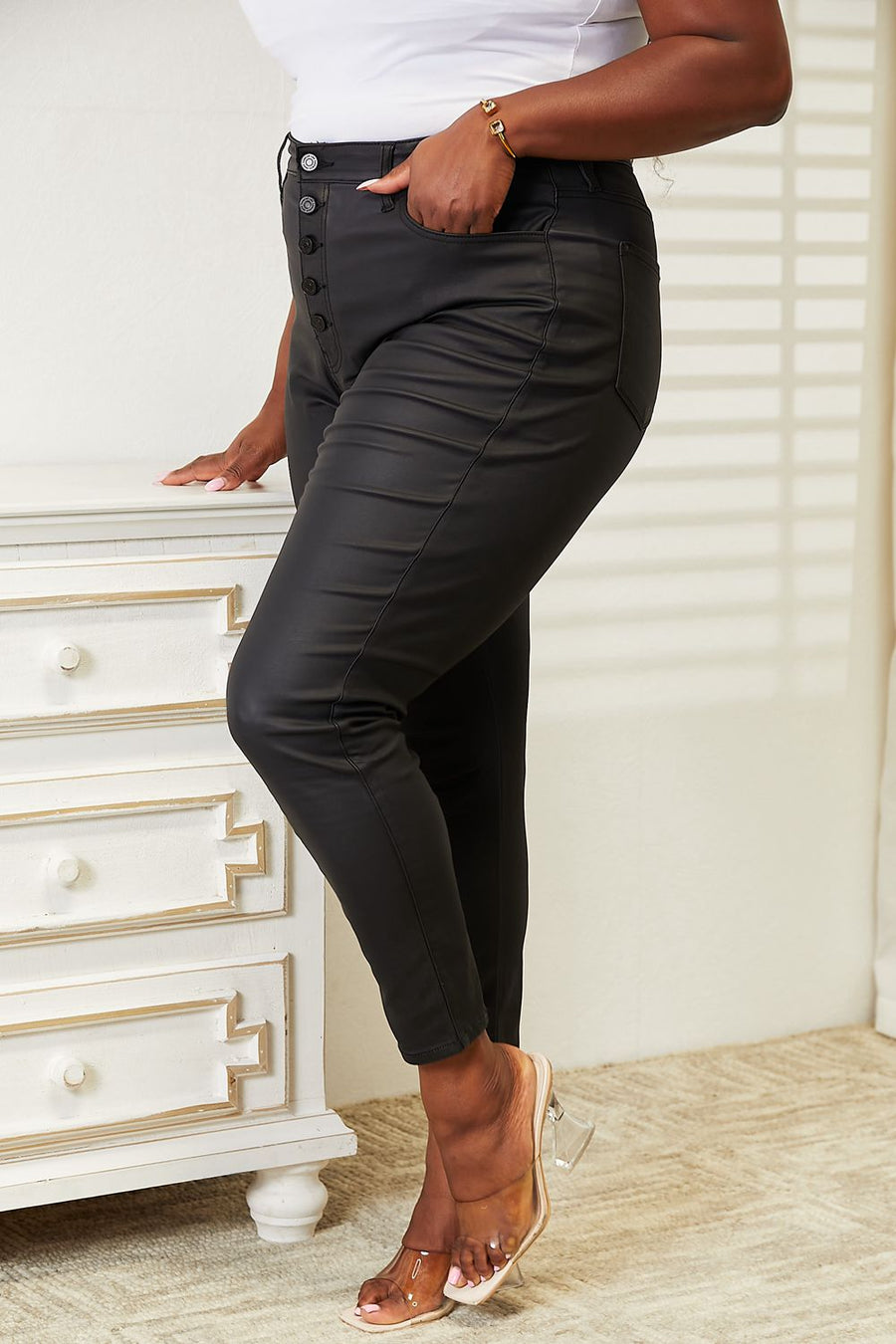 Person wearing black pants with buttons in a room with a white dresser.