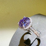 Purple gemstone ring with diamond accents on a gray stand against a yellow background