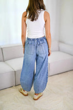 Person wearing a white sleeveless top and blue wide-leg jeans in a minimalistic room.