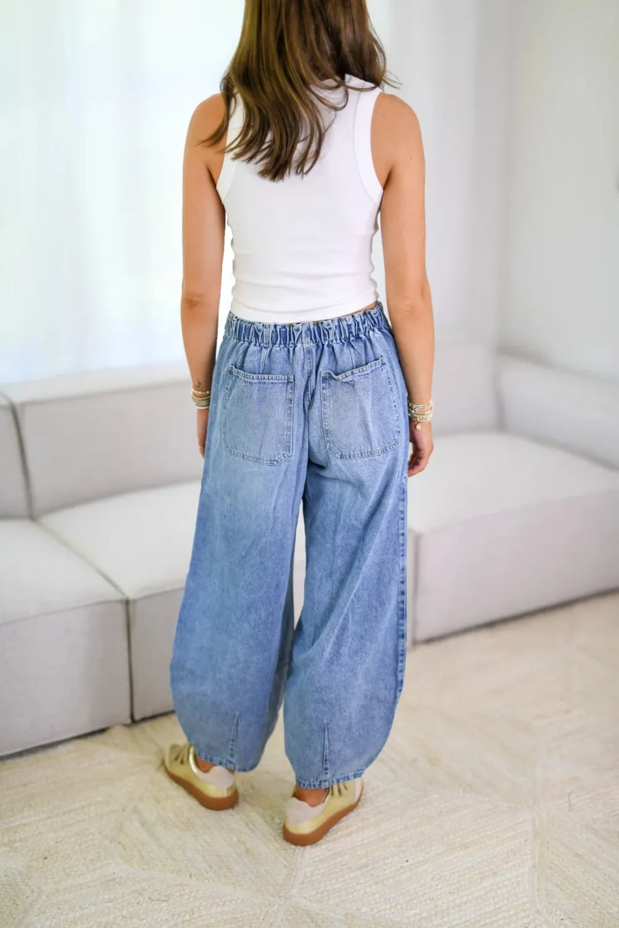 Person wearing a white sleeveless top and blue wide-leg jeans in a minimalistic room.
