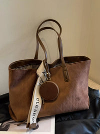 Brown leather handbag with a strap and tag on a light-colored surface
