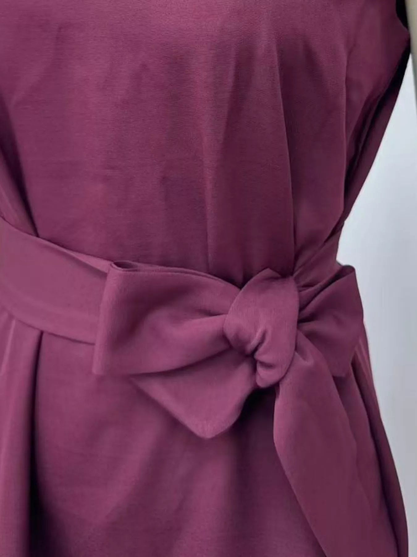 Close-up of a maroon dress with a bow detail on a white background