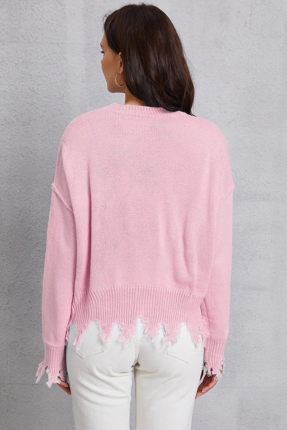 Person wearing a pink sweater with distressed edges against a gray background