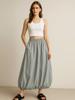 Woman wearing a white tank top and gray skirt on a beige background
