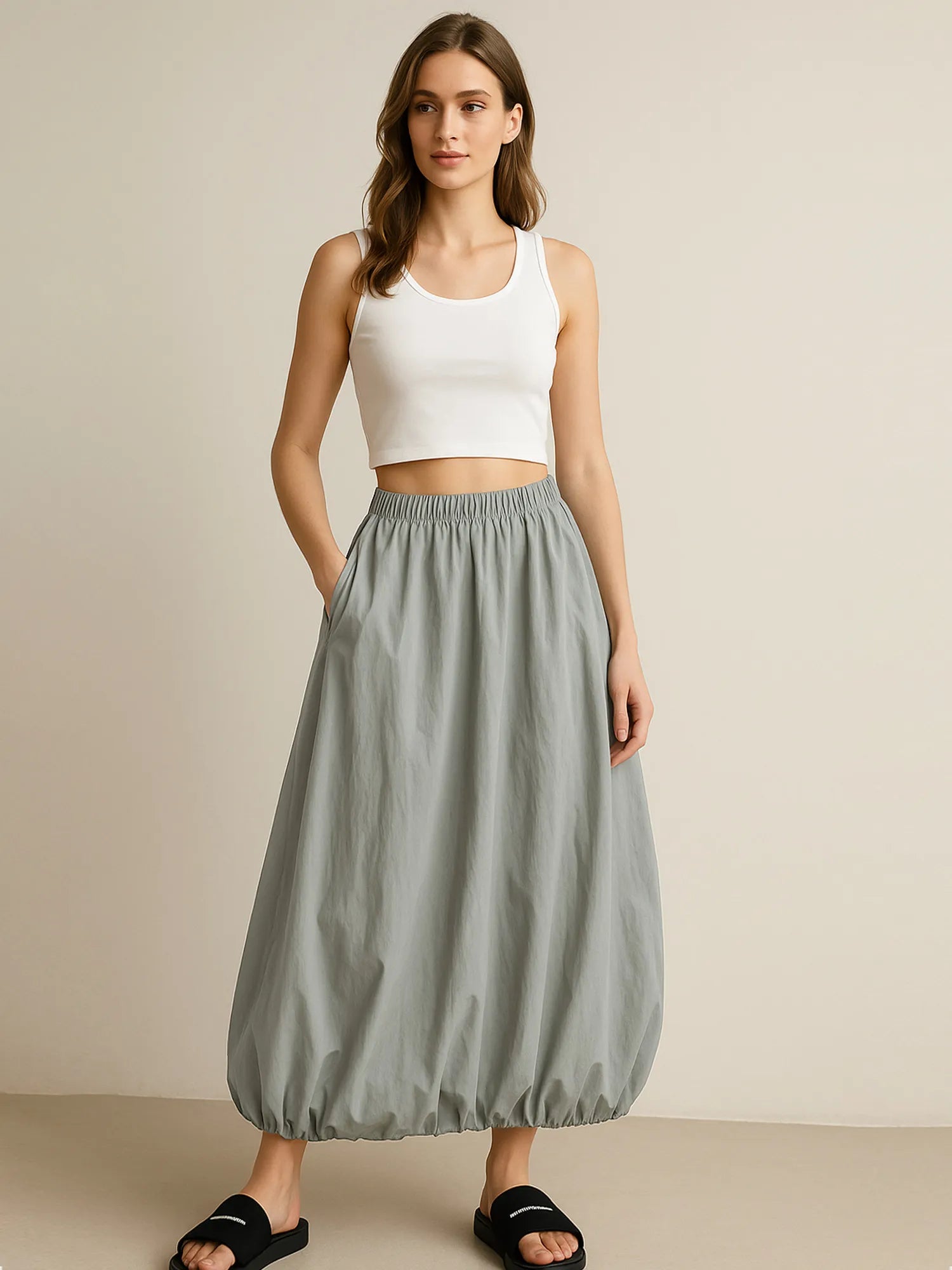 Woman wearing a white tank top and gray skirt on a beige background