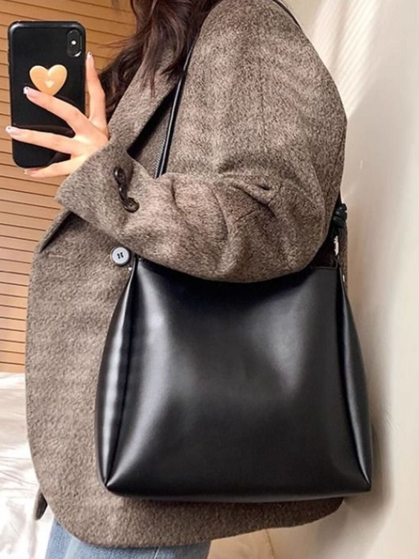 Person holding a black handbag with a neutral background