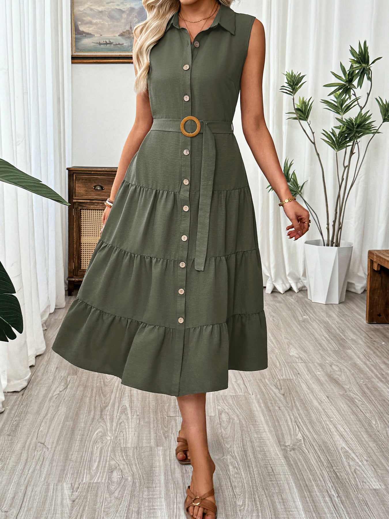 Woman wearing a green dress with a belt in a room with plants and furniture.