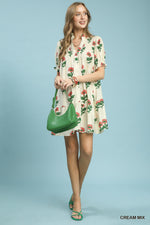 Woman wearing a floral dress holding a green handbag against a light blue background
