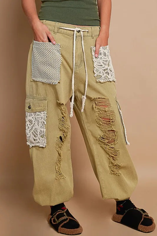 Person wearing beige cargo pants with lace patches on a beige background