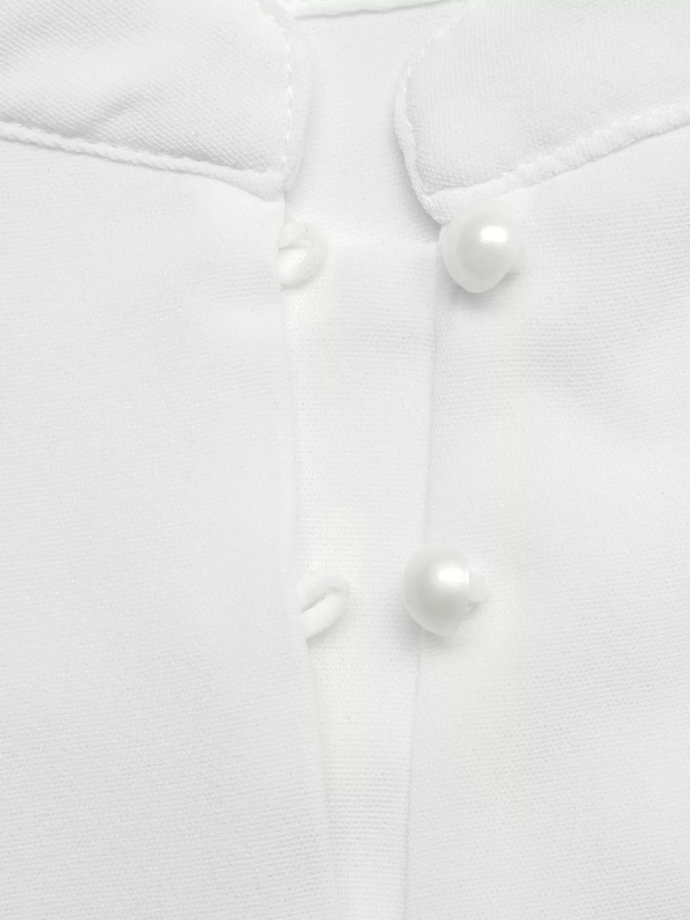 Close-up of a white buttoned shirt with pearl-like buttons on a light gray background