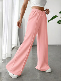 Person wearing pink wide-leg pants and white top in a minimal indoor setting