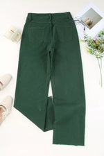 Green pants on a white surface with a floral arrangement and shoes in the background